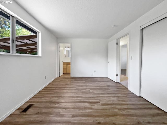 unfurnished bedroom with a textured ceiling, hardwood / wood-style flooring, and connected bathroom