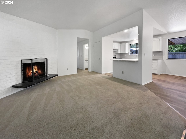 unfurnished living room with light hardwood / wood-style floors, a textured ceiling, and a brick fireplace