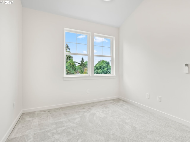 empty room featuring baseboards, vaulted ceiling, and light colored carpet