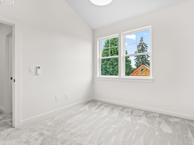 spare room with vaulted ceiling, baseboards, and light colored carpet