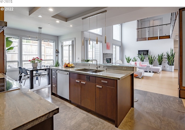 kitchen with an island with sink, stainless steel dishwasher, hanging light fixtures, and sink