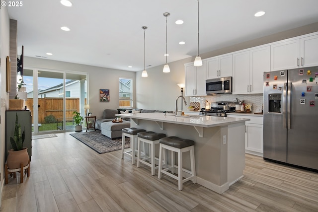 kitchen featuring appliances with stainless steel finishes, pendant lighting, a center island with sink, light hardwood / wood-style floors, and white cabinetry