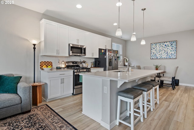 kitchen with sink, an island with sink, decorative light fixtures, white cabinetry, and stainless steel appliances