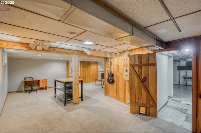 finished basement with a paneled ceiling, carpet floors, wooden walls, and baseboards
