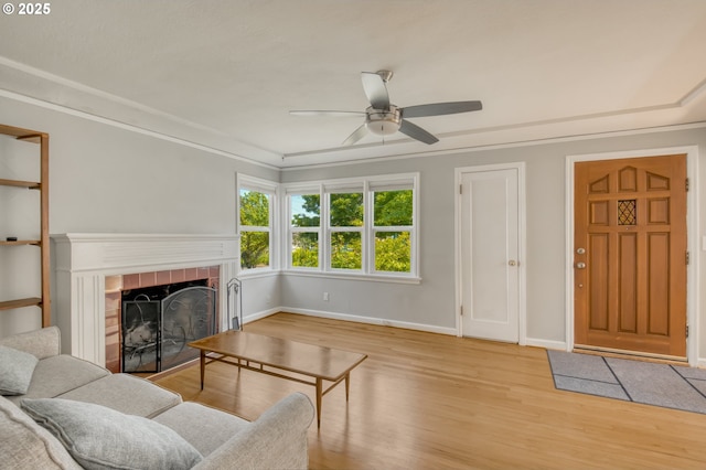 living room with wood finished floors, a fireplace, ceiling fan, baseboards, and ornamental molding