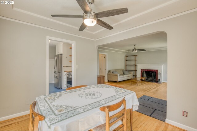 bedroom featuring freestanding refrigerator, arched walkways, light wood finished floors, a brick fireplace, and baseboards