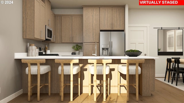 kitchen featuring stainless steel appliances, a kitchen bar, light brown cabinets, and light wood-type flooring