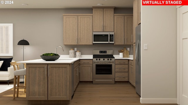 kitchen with sink, wood-type flooring, kitchen peninsula, and appliances with stainless steel finishes