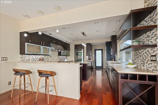 kitchen featuring range hood, backsplash, kitchen peninsula, pendant lighting, and a breakfast bar