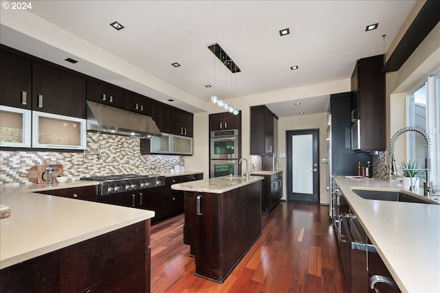 kitchen featuring a center island with sink, sink, hanging light fixtures, appliances with stainless steel finishes, and tasteful backsplash