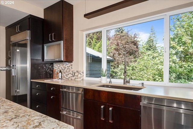 kitchen with decorative backsplash, light stone counters, dark brown cabinets, and stainless steel appliances