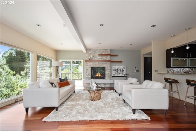 living room featuring beam ceiling, a stone fireplace, a wealth of natural light, and hardwood / wood-style flooring