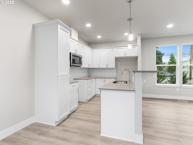 kitchen with white cabinetry, decorative backsplash, hanging light fixtures, and an island with sink