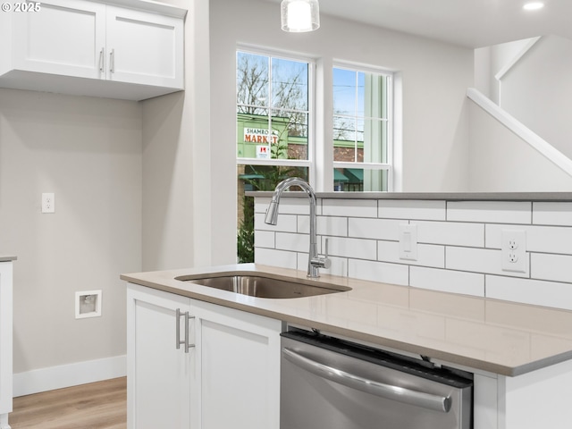 kitchen featuring tasteful backsplash, dishwasher, sink, white cabinetry, and light stone countertops