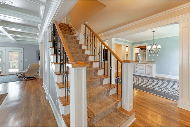 staircase featuring coffered ceiling, wood-type flooring, ornamental molding, french doors, and a chandelier