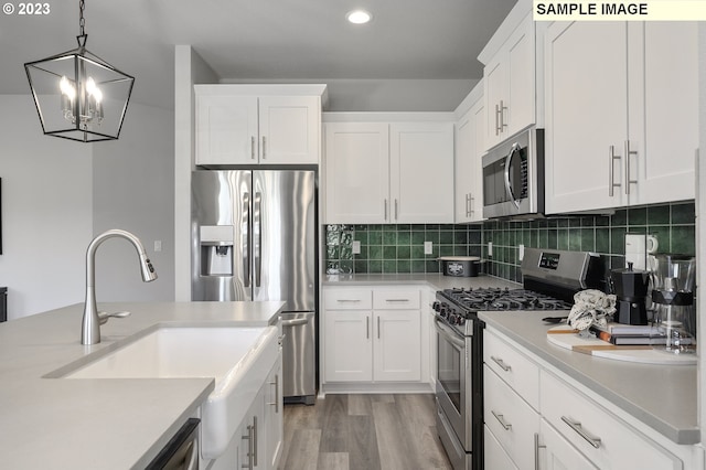 kitchen featuring white cabinets, stainless steel appliances, decorative light fixtures, and light wood-type flooring