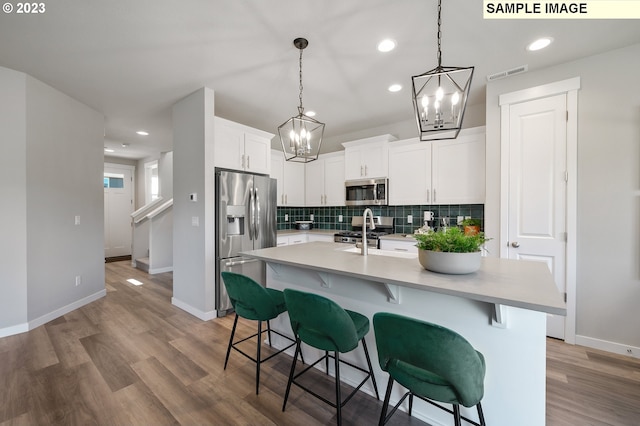 kitchen with stainless steel appliances, a kitchen breakfast bar, light hardwood / wood-style floors, a kitchen island with sink, and white cabinets