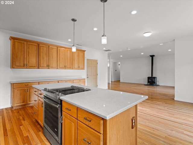 kitchen with a kitchen island, light hardwood / wood-style flooring, a wood stove, pendant lighting, and stainless steel range oven