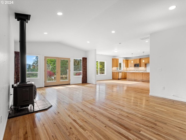 unfurnished living room with lofted ceiling, a wood stove, light hardwood / wood-style flooring, and plenty of natural light