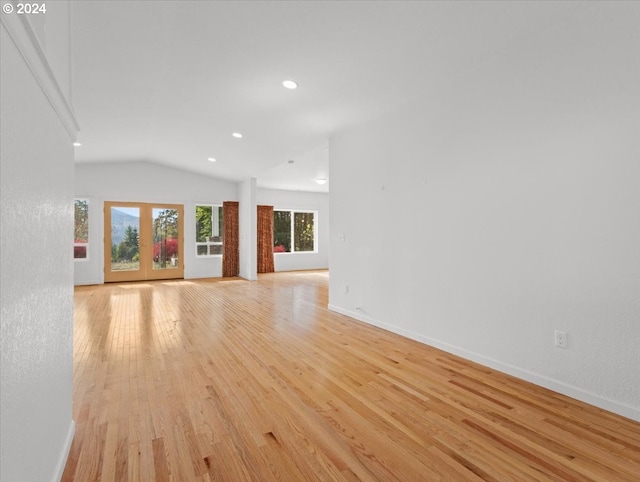 unfurnished living room with vaulted ceiling, light hardwood / wood-style flooring, and french doors