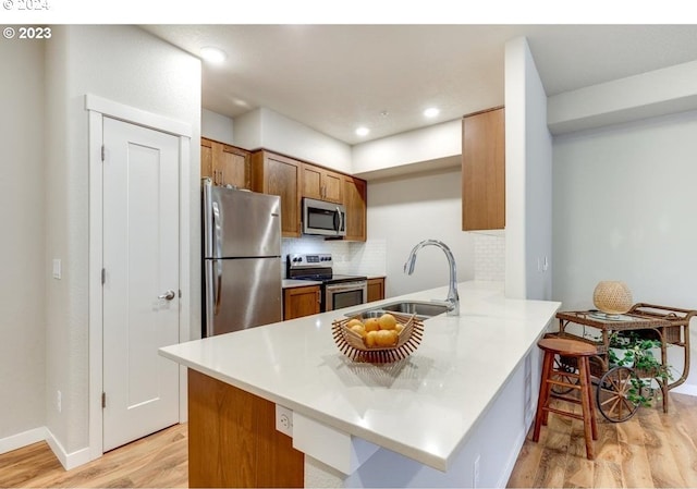 kitchen with light hardwood / wood-style flooring, appliances with stainless steel finishes, tasteful backsplash, kitchen peninsula, and a breakfast bar area