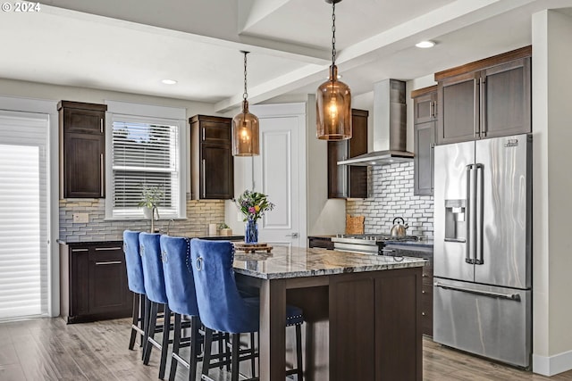 kitchen with a kitchen island, high end fridge, light hardwood / wood-style floors, wall chimney range hood, and hanging light fixtures