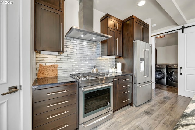 kitchen with wall chimney exhaust hood, a barn door, light hardwood / wood-style floors, washing machine and clothes dryer, and high quality appliances