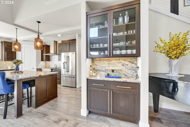 kitchen featuring light stone countertops, tasteful backsplash, wall chimney range hood, decorative light fixtures, and stainless steel refrigerator with ice dispenser