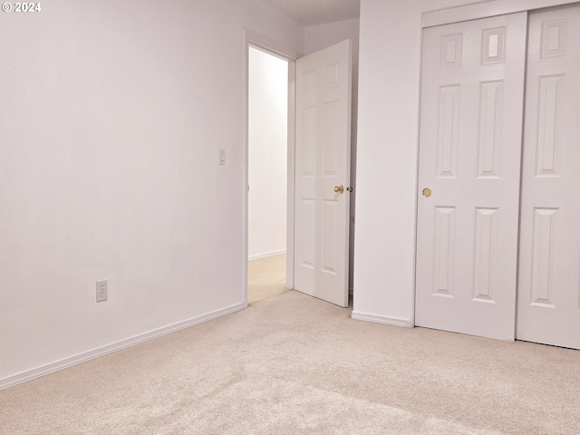 unfurnished bedroom with light colored carpet and a closet