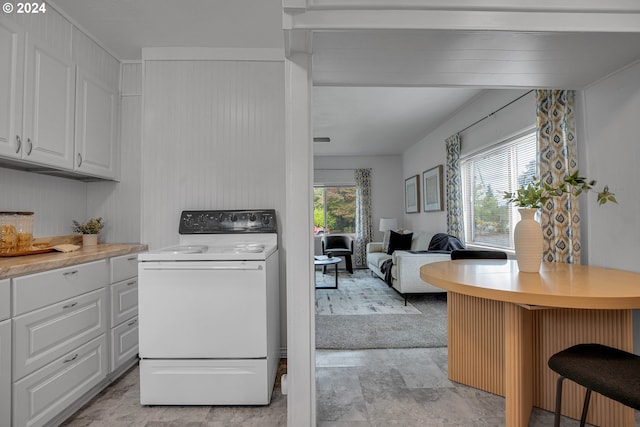 kitchen featuring a kitchen breakfast bar, white range oven, white cabinets, and plenty of natural light