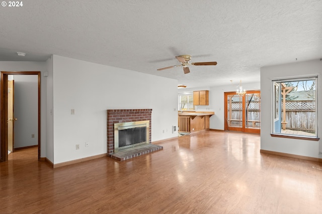 unfurnished living room featuring hardwood / wood-style floors, a healthy amount of sunlight, ceiling fan with notable chandelier, and a brick fireplace