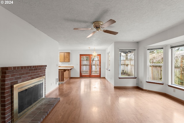 unfurnished living room with a fireplace, a textured ceiling, light wood-type flooring, and ceiling fan with notable chandelier