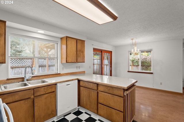 kitchen with white dishwasher, sink, decorative light fixtures, kitchen peninsula, and a chandelier