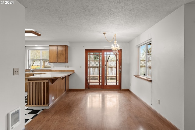 kitchen with kitchen peninsula, pendant lighting, an inviting chandelier, and a healthy amount of sunlight