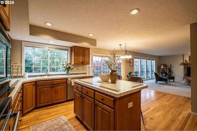 kitchen featuring dishwasher, sink, tile countertops, pendant lighting, and a kitchen island