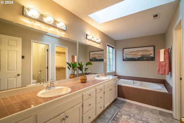 bathroom with a skylight, vanity, tiled tub, and toilet