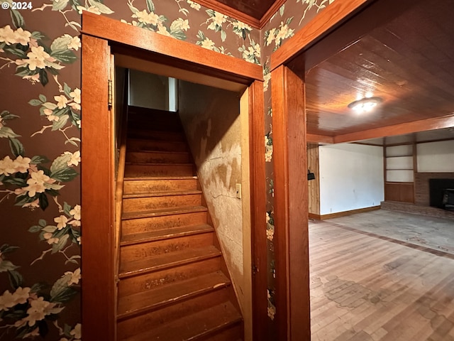 staircase featuring wallpapered walls, baseboards, wood ceiling, a fireplace, and wood finished floors