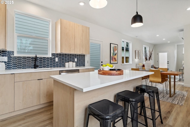 kitchen with a center island, light countertops, hanging light fixtures, light brown cabinets, and a sink