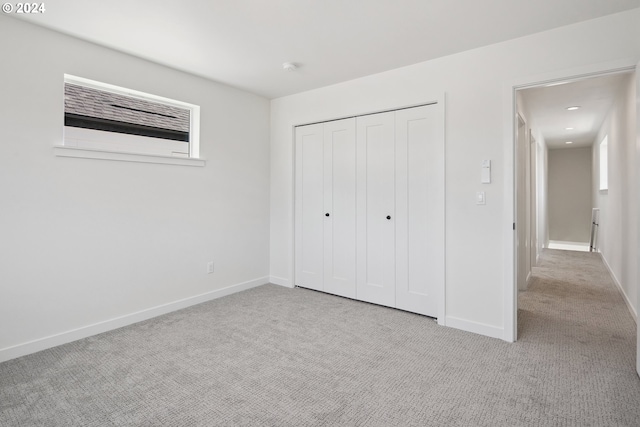 unfurnished bedroom with a closet, light colored carpet, and baseboards