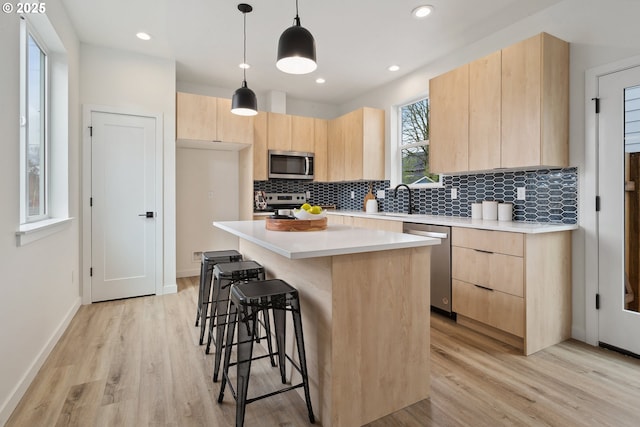 kitchen featuring light countertops, appliances with stainless steel finishes, light brown cabinetry, and a center island