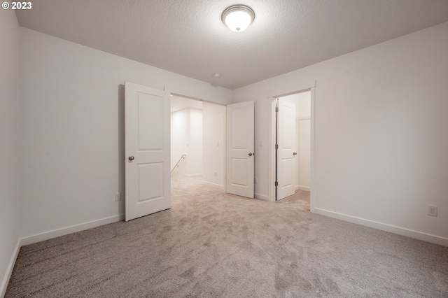 unfurnished bedroom with light carpet, a textured ceiling, a walk in closet, and a closet