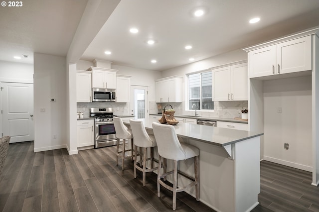 kitchen with appliances with stainless steel finishes, dark hardwood / wood-style flooring, a breakfast bar, a kitchen island, and white cabinetry