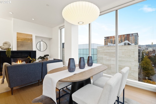 dining space with a fireplace, a wall of windows, and light hardwood / wood-style flooring