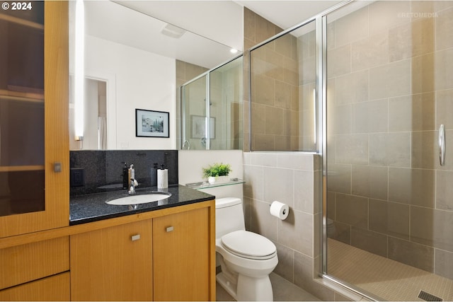 bathroom featuring toilet, tile walls, tasteful backsplash, vanity, and a shower with shower door