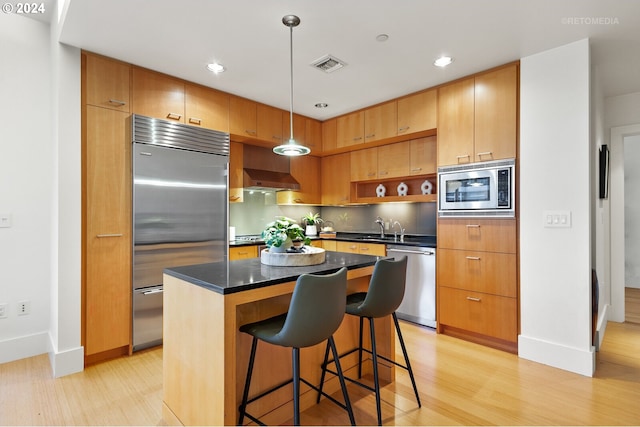 kitchen featuring built in appliances, sink, hanging light fixtures, light hardwood / wood-style flooring, and a center island