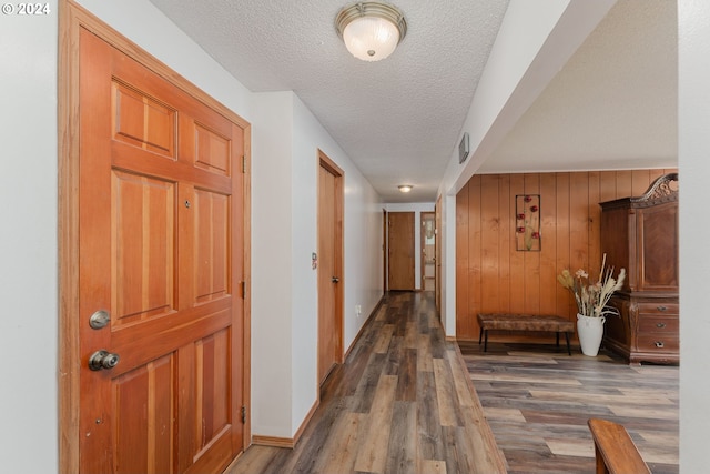 corridor featuring a textured ceiling, wood walls, and dark hardwood / wood-style flooring