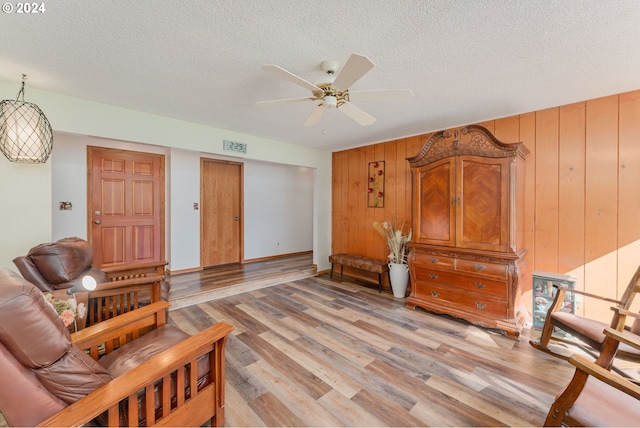 living room featuring light wood-type flooring, a textured ceiling, wood walls, and ceiling fan