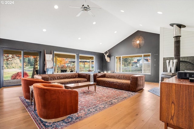 living room featuring light hardwood / wood-style floors, a wood stove, lofted ceiling, and ceiling fan