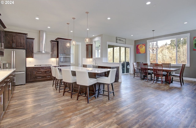 kitchen featuring wall chimney range hood, decorative light fixtures, a notable chandelier, dark brown cabinets, and stainless steel appliances