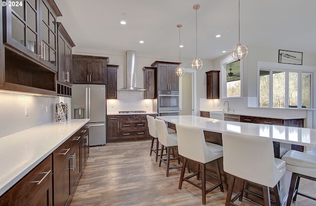 kitchen with dark brown cabinetry, decorative light fixtures, wall chimney range hood, and appliances with stainless steel finishes